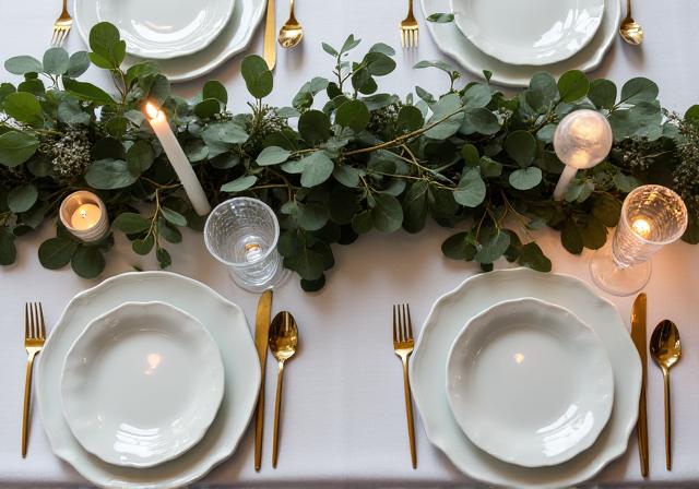 A beautifully set wedding table featuring lush eucalyptus runners, delicate place settings, and warm candlelight.